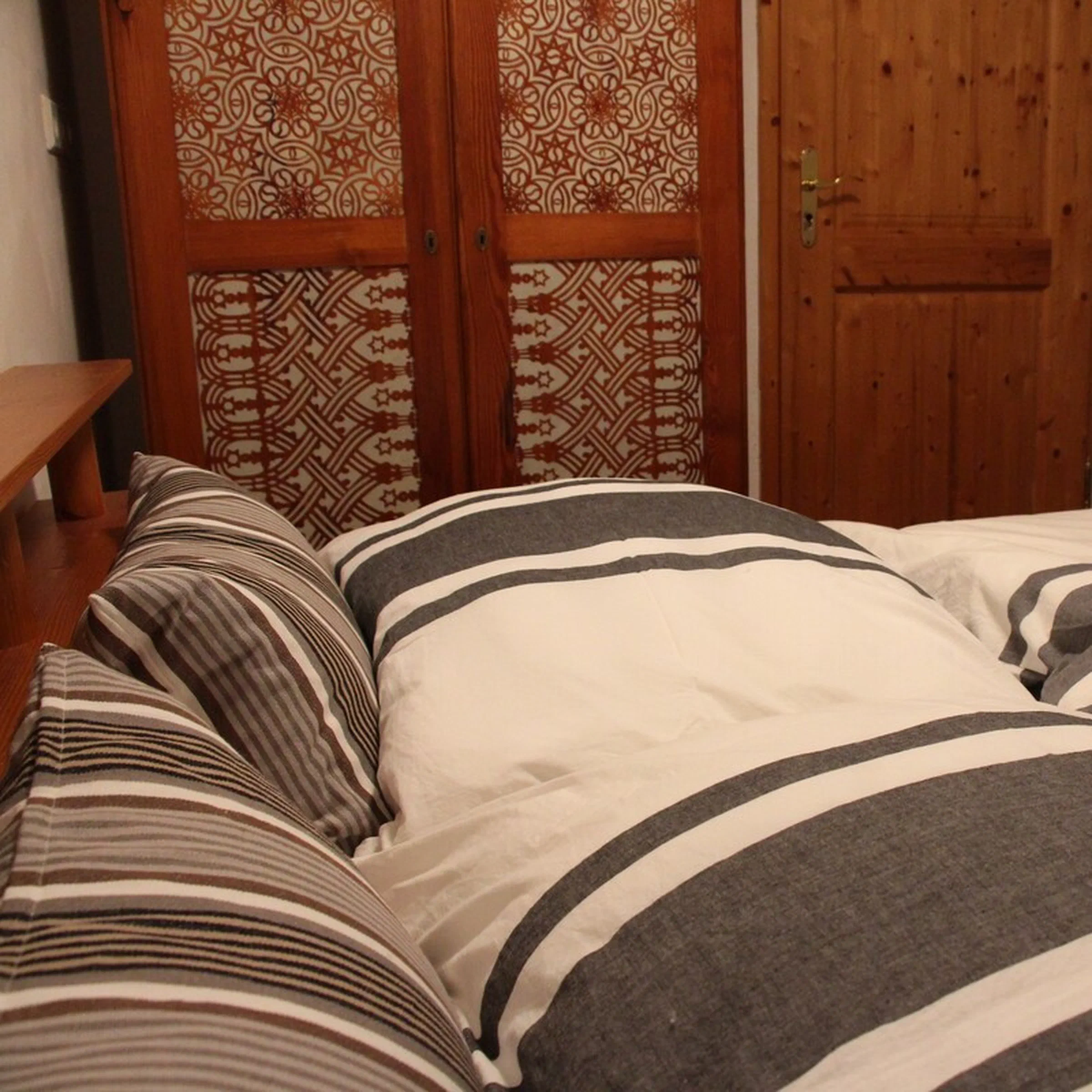 Schlafzimmer von Fewo 3 mit gestreifter Bettwäsche und antikem Schrank