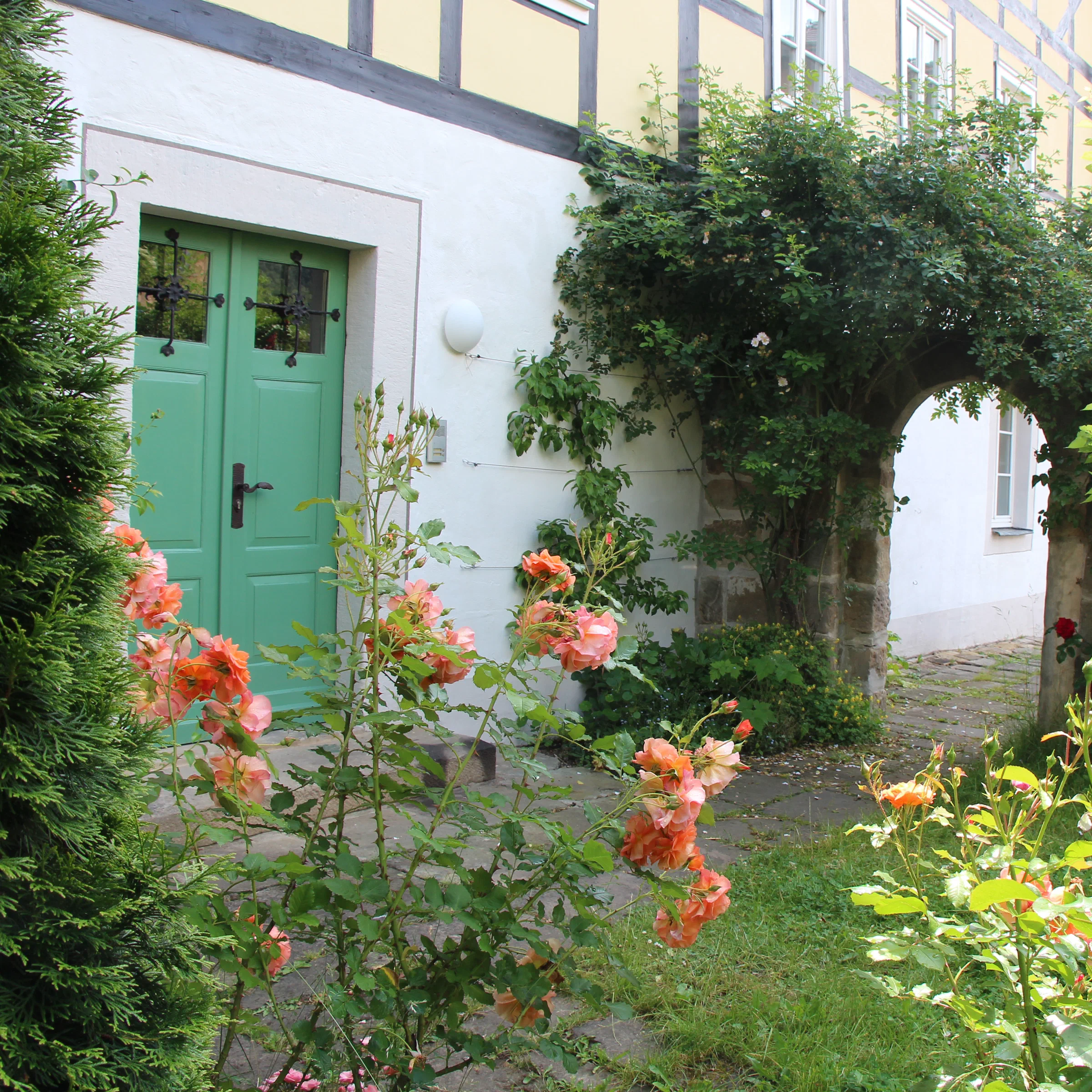 Grüne Gartentür mit Rosen und Steinbogen im Garten